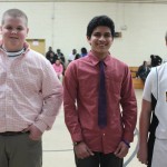 Three boys in ties standing in a gym.