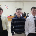 Three boys in ties standing in a gym.