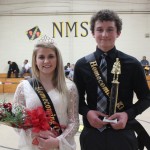 Two young athletes proudly holding trophies in a gym.