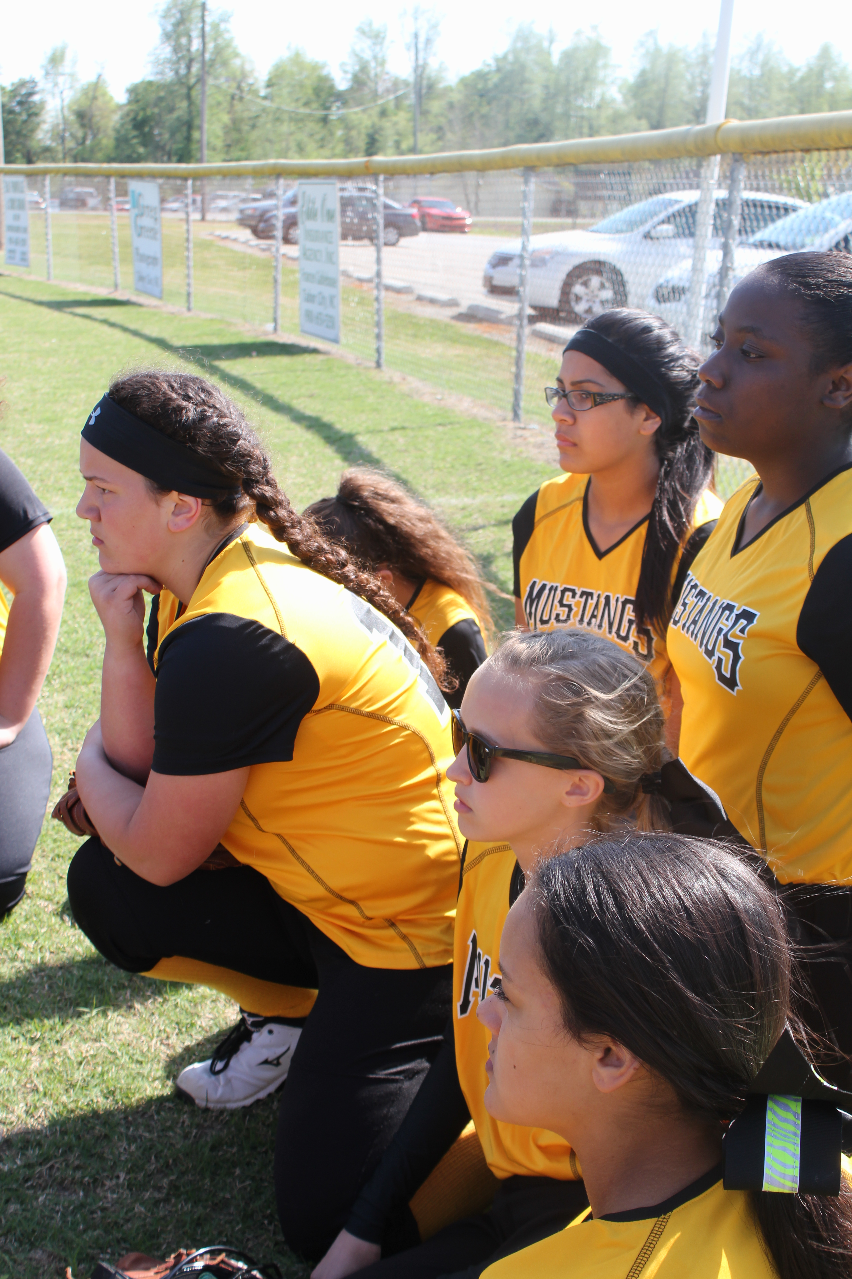 A team of softball players sitting on the grass field, taking a break during a game.