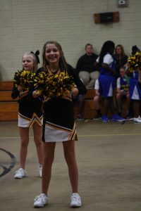 Cheerleaders in black and yellow uniforms standing on a court, ready to perform energetic routines.