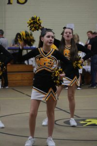 Cheerleaders in uniform performing energetic routine on basketball court during game.