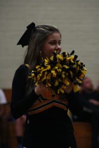 A cheerleader in a black and yellow uniform performing a routine at a sports event.