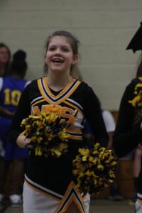 Cheerleaders in black and yellow uniforms smiling and cheering at a sporting event.