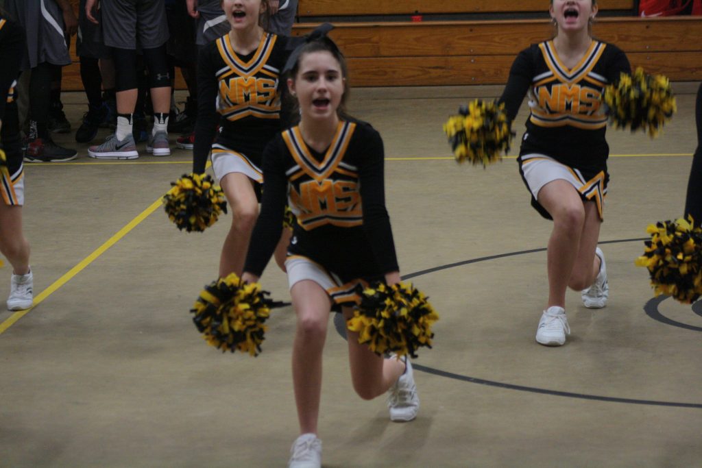 Cheerleaders in colorful uniforms perform energetic routines on the basketball court.