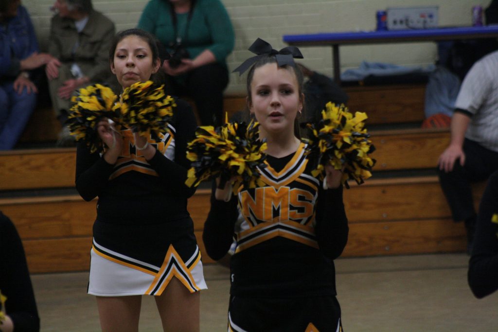 Two cheerleaders in black and yellow uniforms standing on the court.