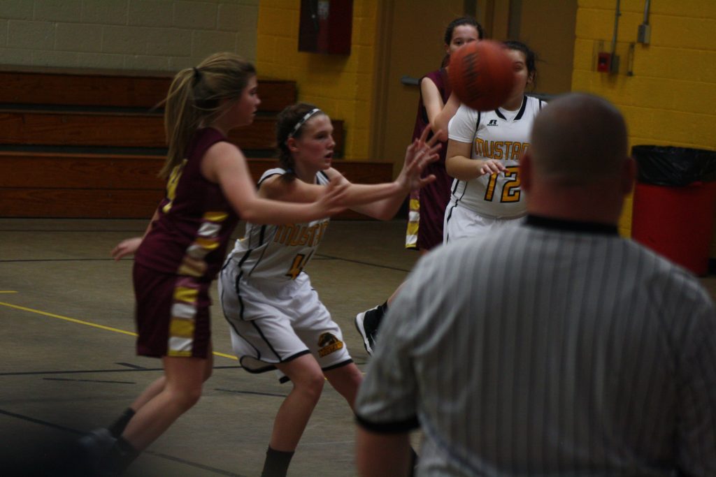 A girl in a yellow and maroon uniform attempting to block a ball during a sports game.