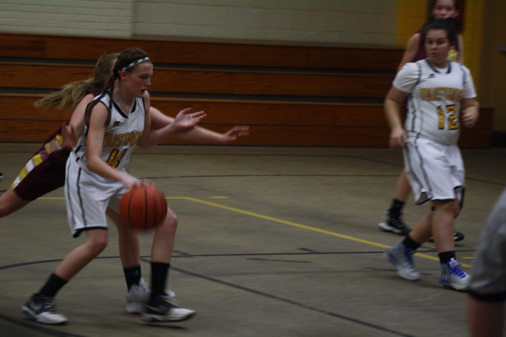 A girl in a white and yellow uniform dribbling a basketball on a basketball court.