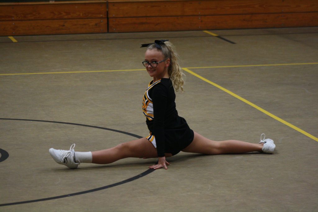 Cheerleader girl in uniform performing a split during a routine.