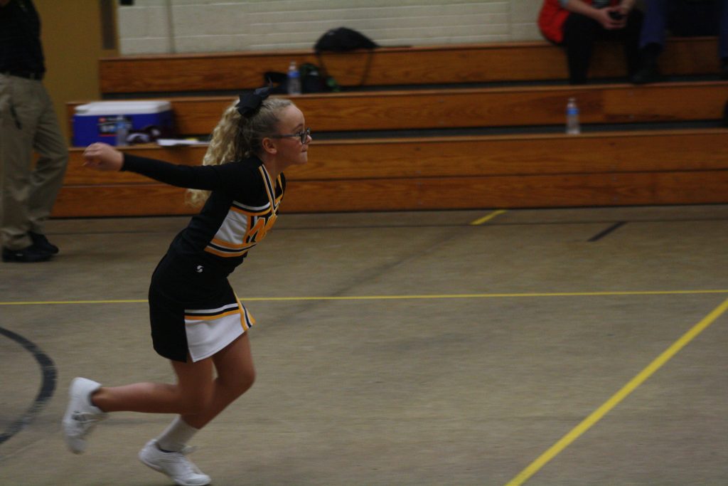 Young cheerleader in mid-air jump, wearing uniform with pom-poms, showcasing athleticism and spirit.