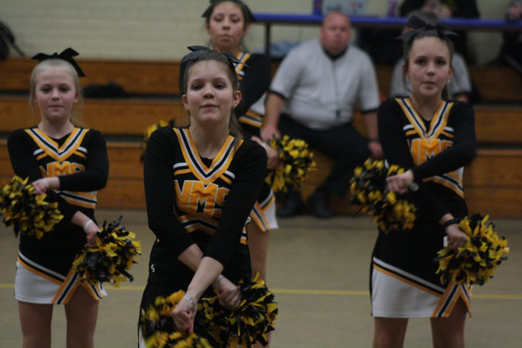 Cheerleaders in colorful uniforms perform energetic routines on the basketball court.