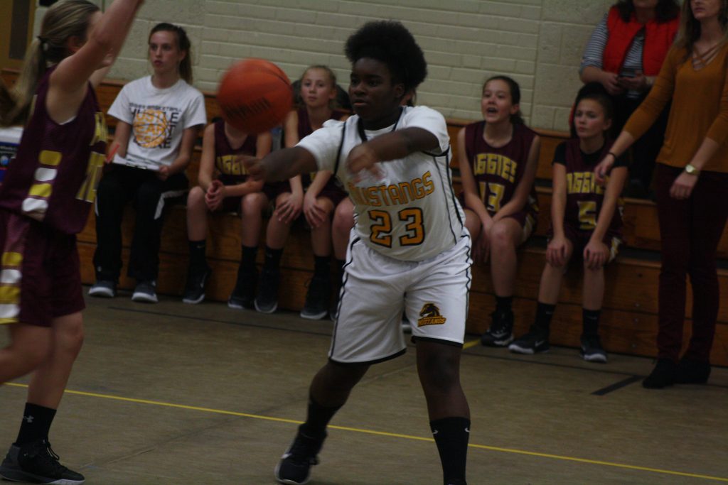 A girl in a white and gold uniform preparing to pass a ball on the field.