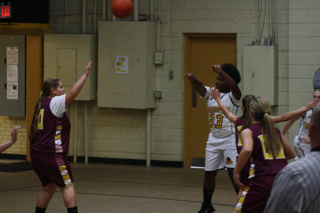 Young female basketball players in action on court during a game in a school gymnasium.