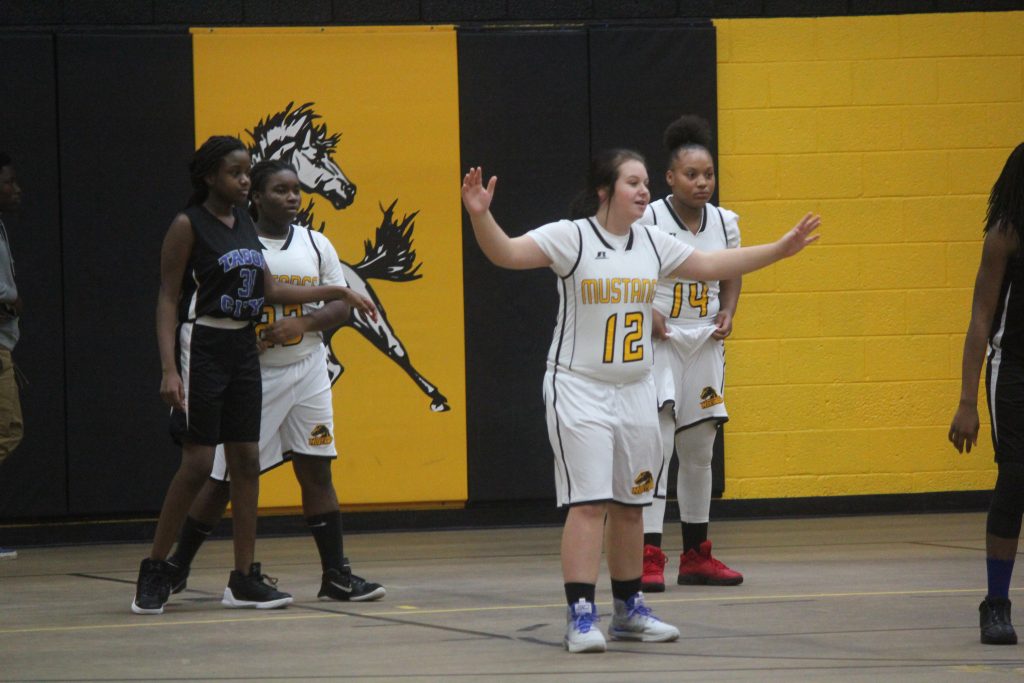 Young female basketball players joyfully celebrate on court after scoring a basket.