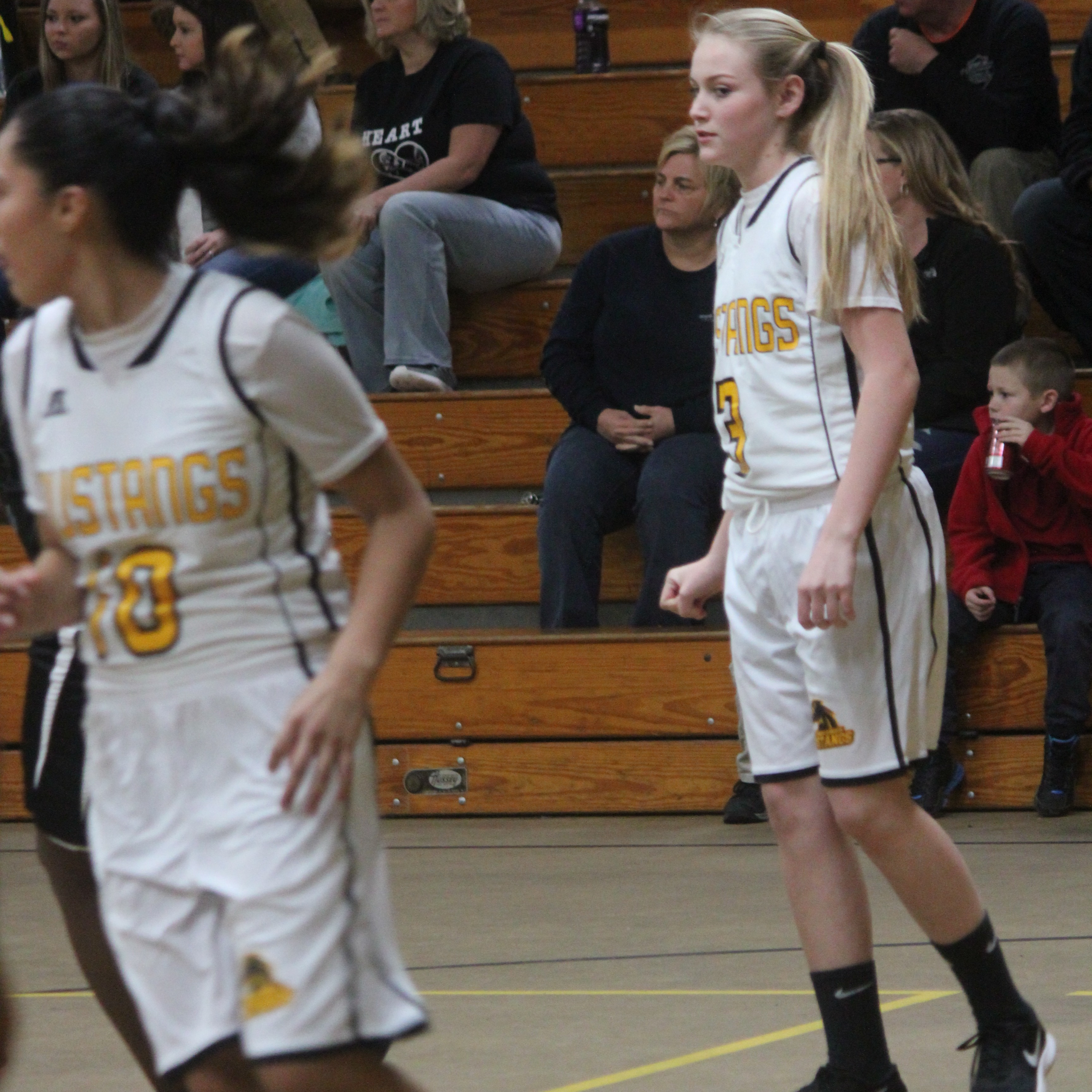 Young female basketball players joyfully celebrate on court after scoring a basket.