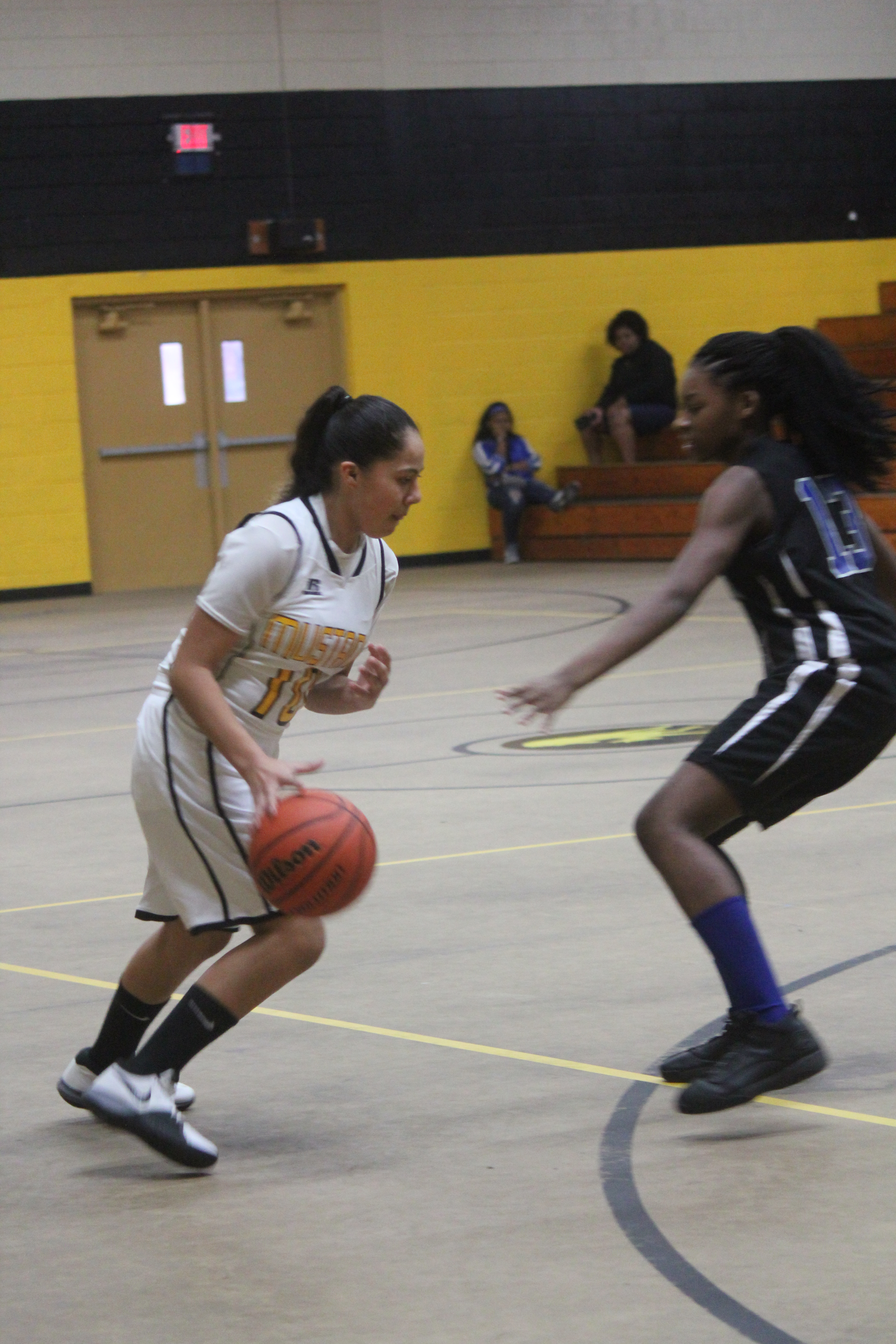 A girl in a white uniform dribbling a basketball on a basketball court.