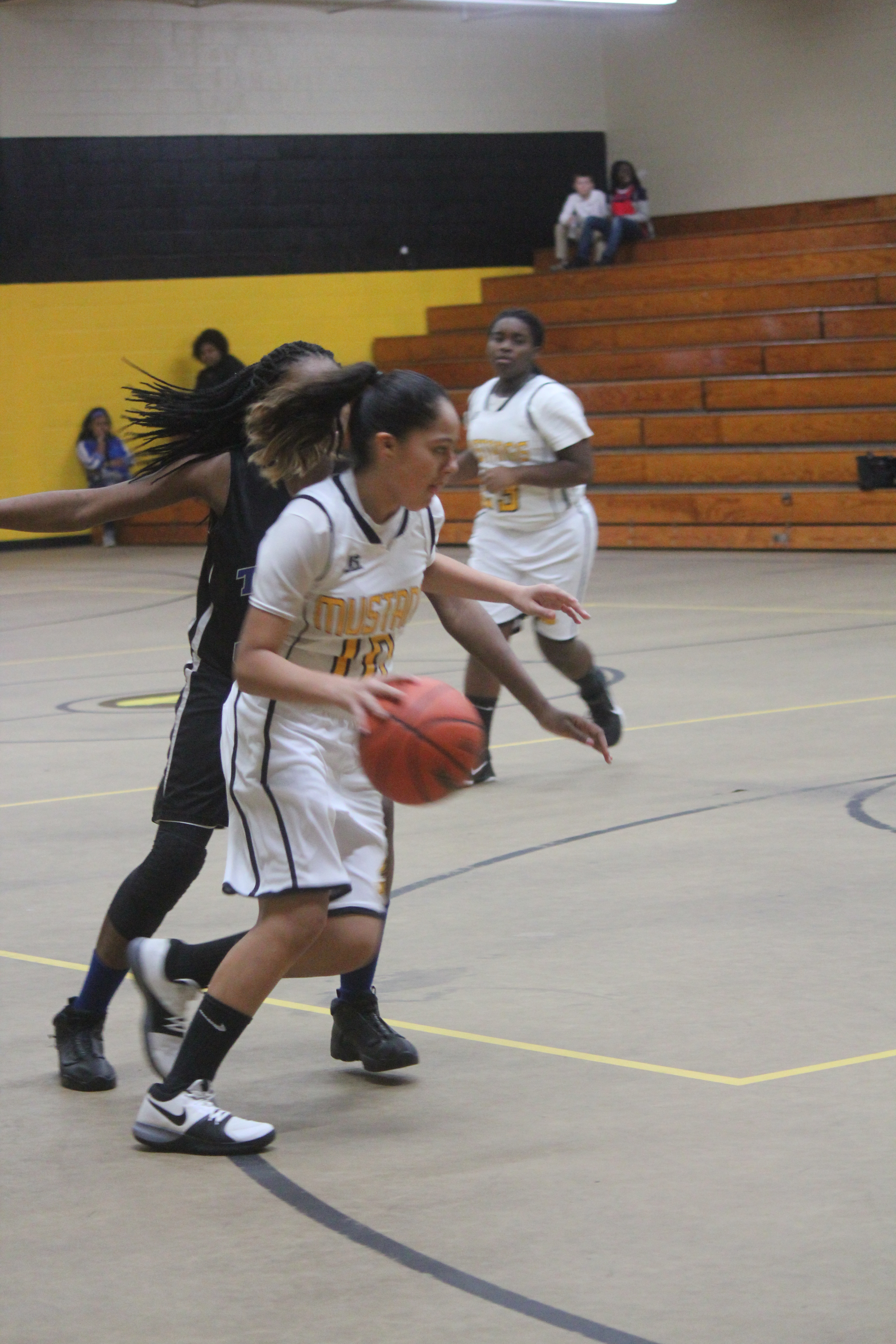 A girl in a white and black uniform dribbling a basketball on a basketball court.