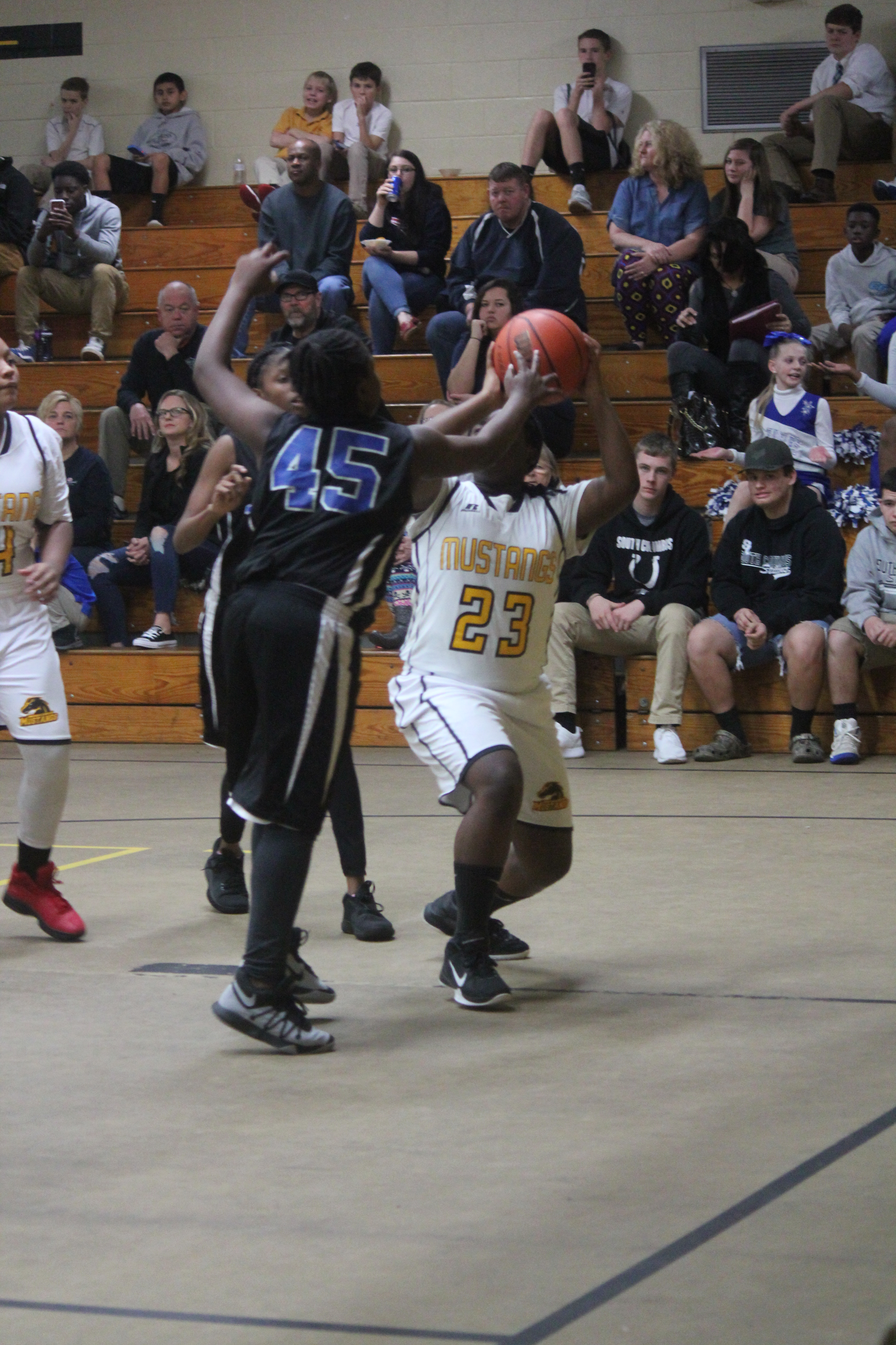 Female basketball player trying to shoot the ball while the other player is trying to block her shot.