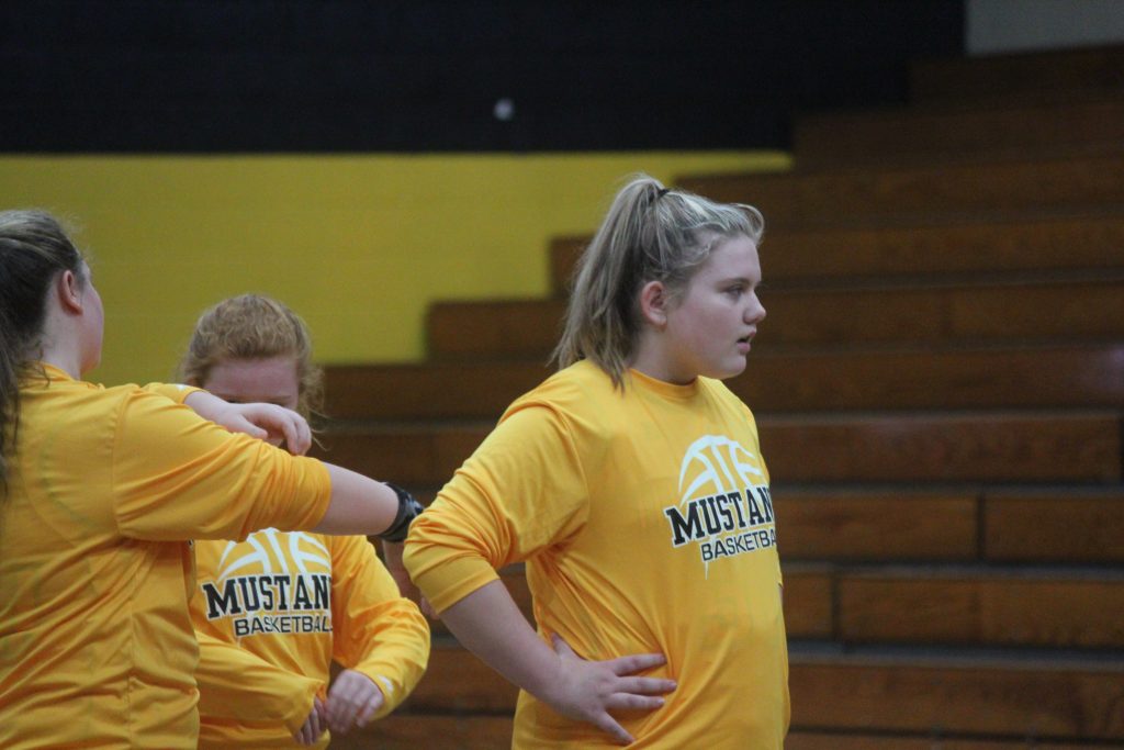 Three girls in yellow shirts standing on a basketball court.