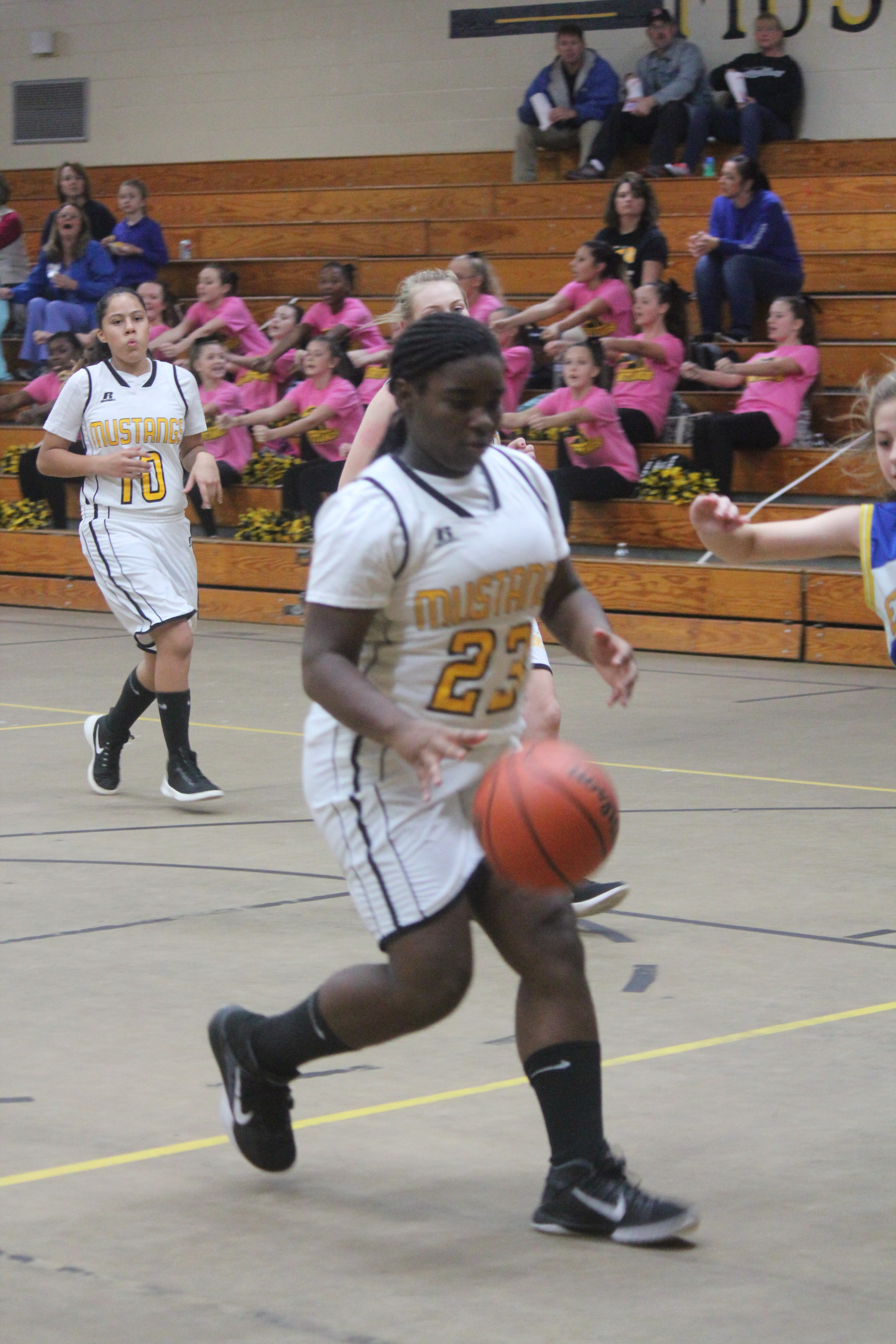 Young female athlete in white and yellow uniform dribbling basketball on court.