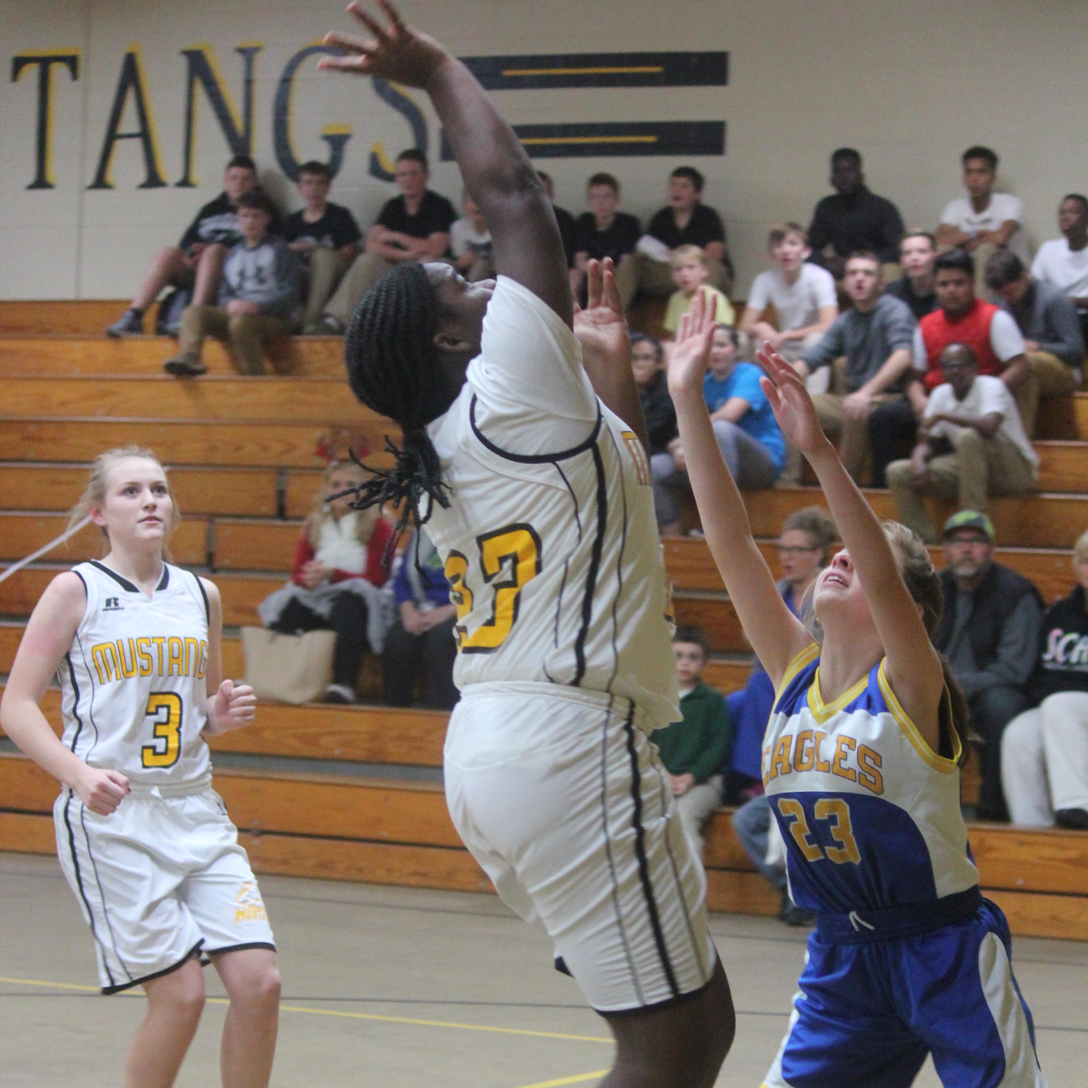 Young female athlete in white and yellow uniform shooting the ball..