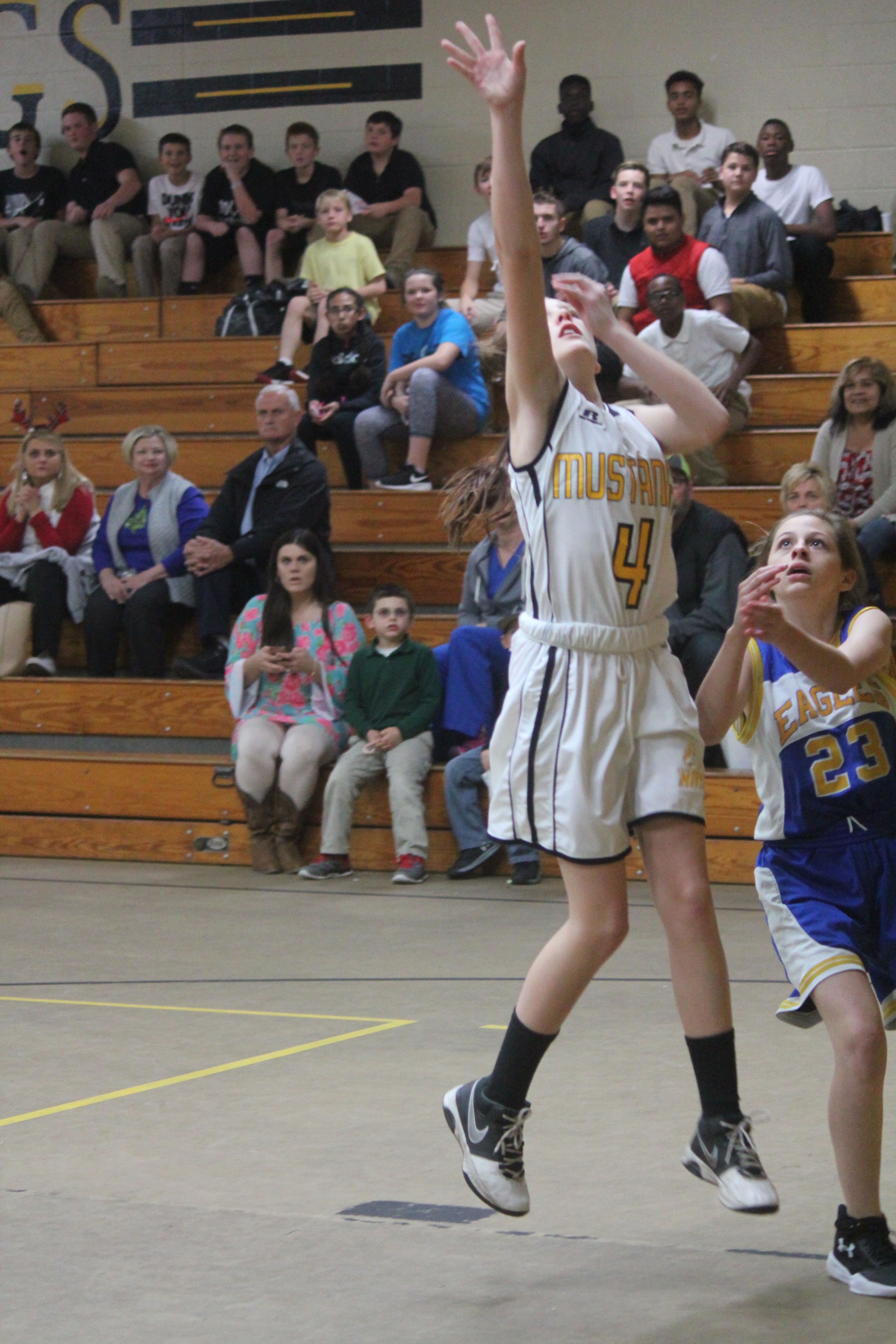 Young female athlete in white and yellow uniform trying to get a rebound.