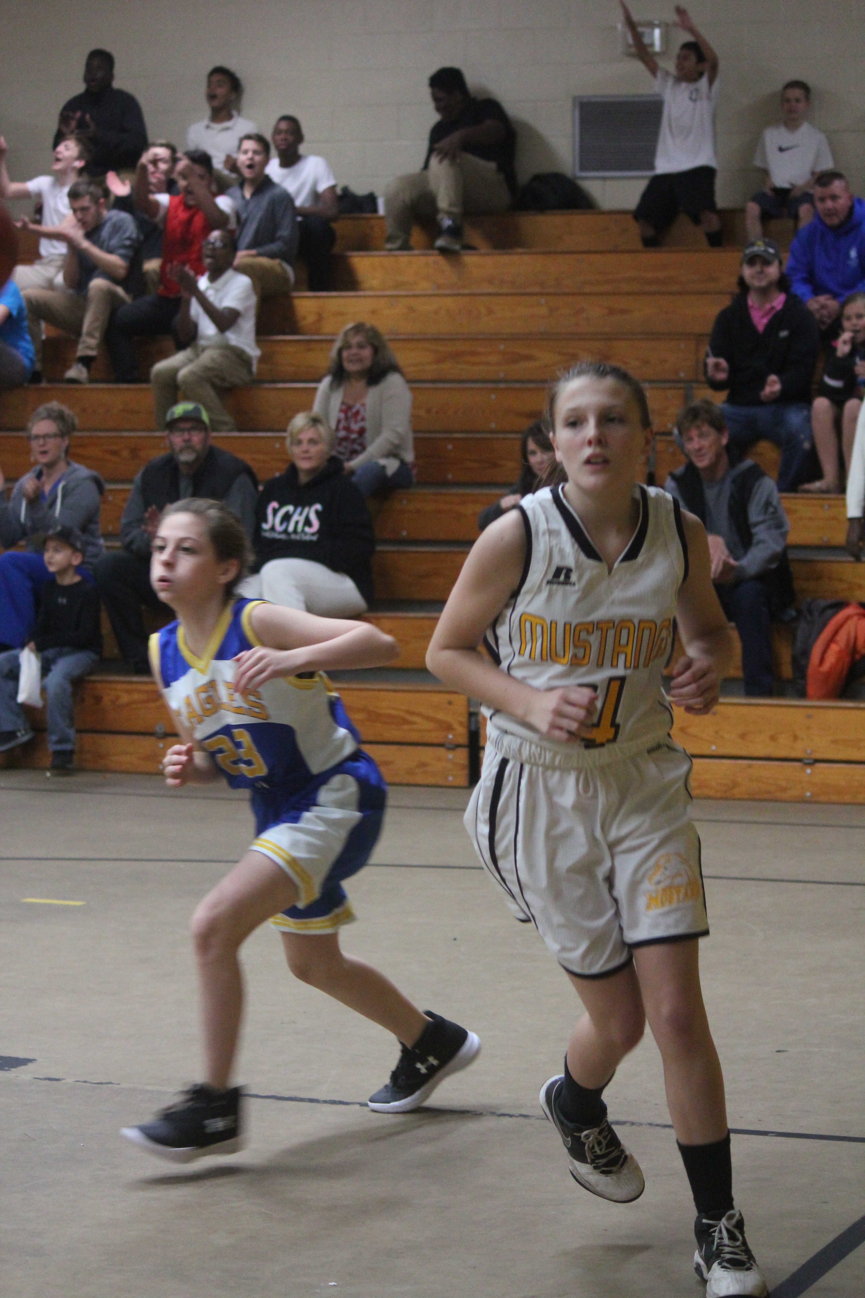 Two female basketball players running inside a basketball court.