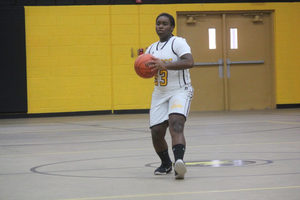 Female basketball player in white and yellow uniform holding a basketball.