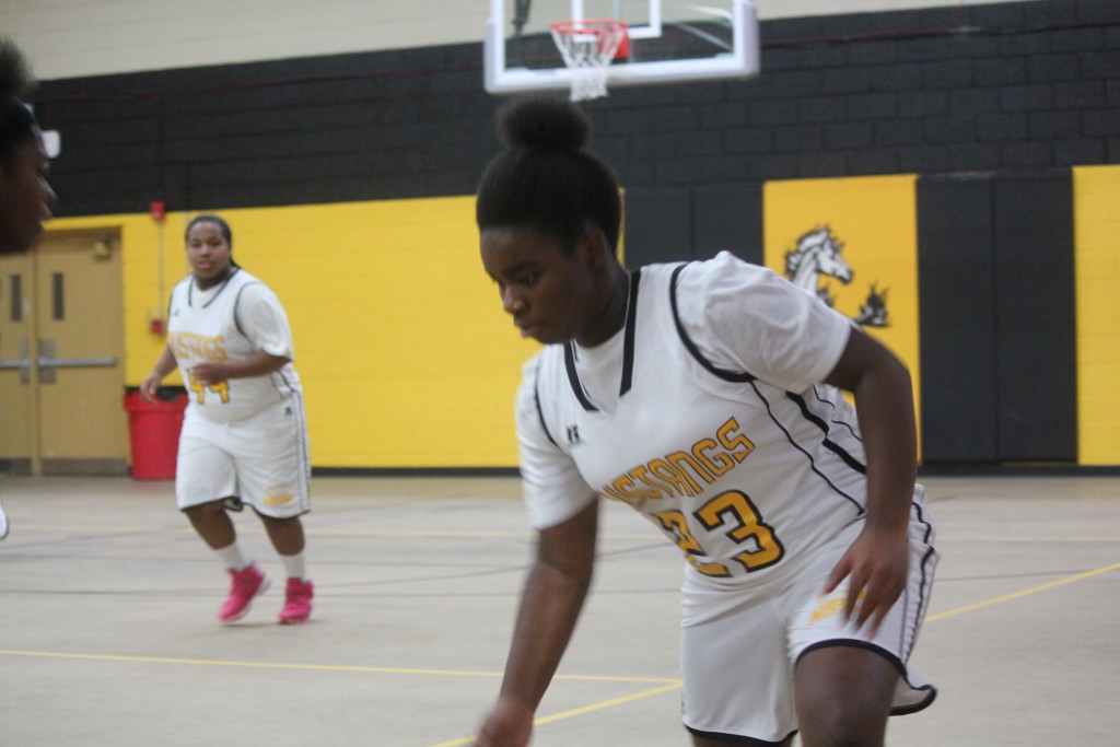 A girl in a white basketball uniform dribbling a basketball on the court.