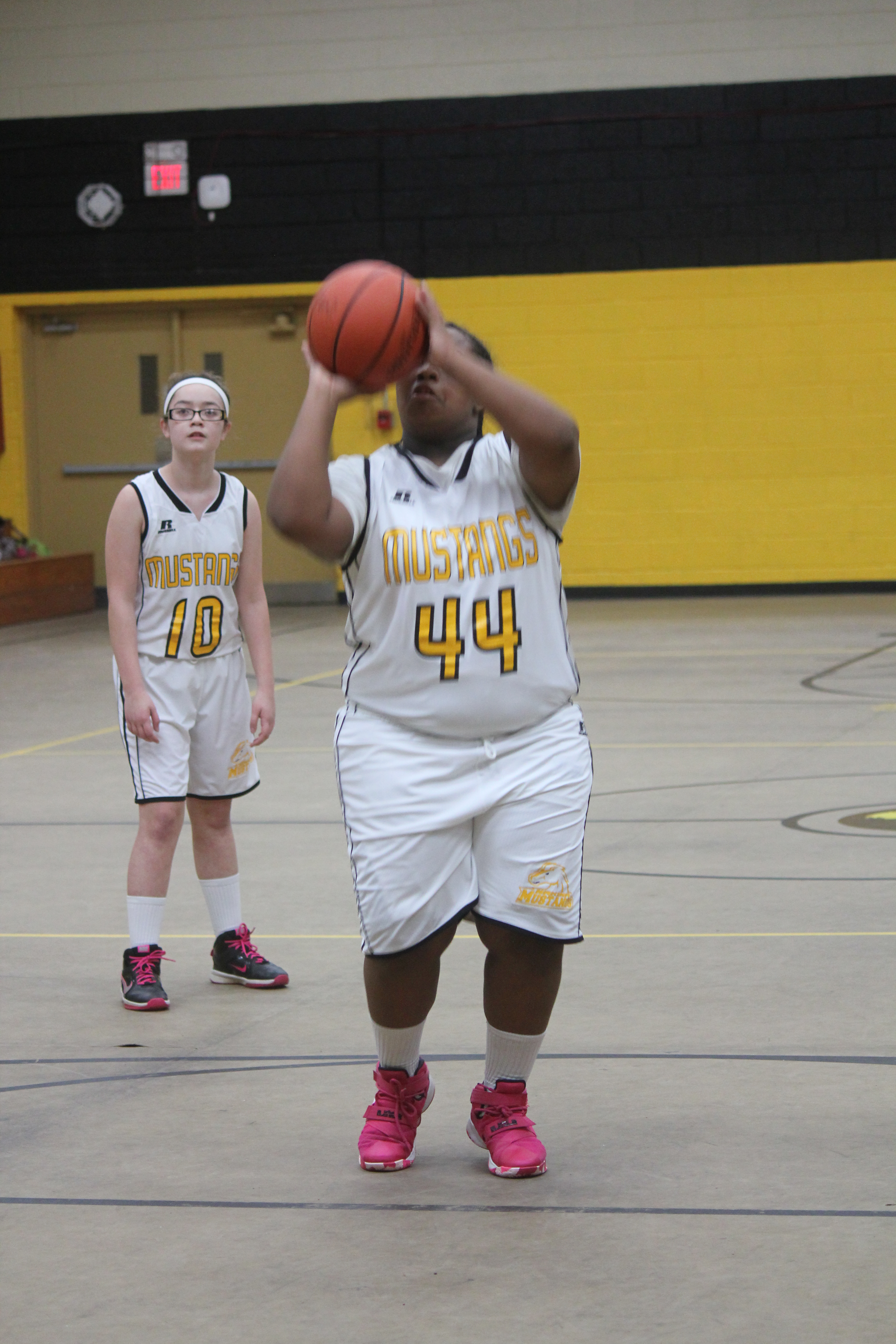 Young female basketball player in white and yellow uniform shooting a basketball on the court.