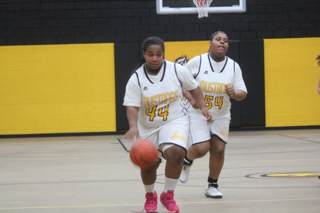 Two girls in white and yellow uniforms playing basketball on a court.