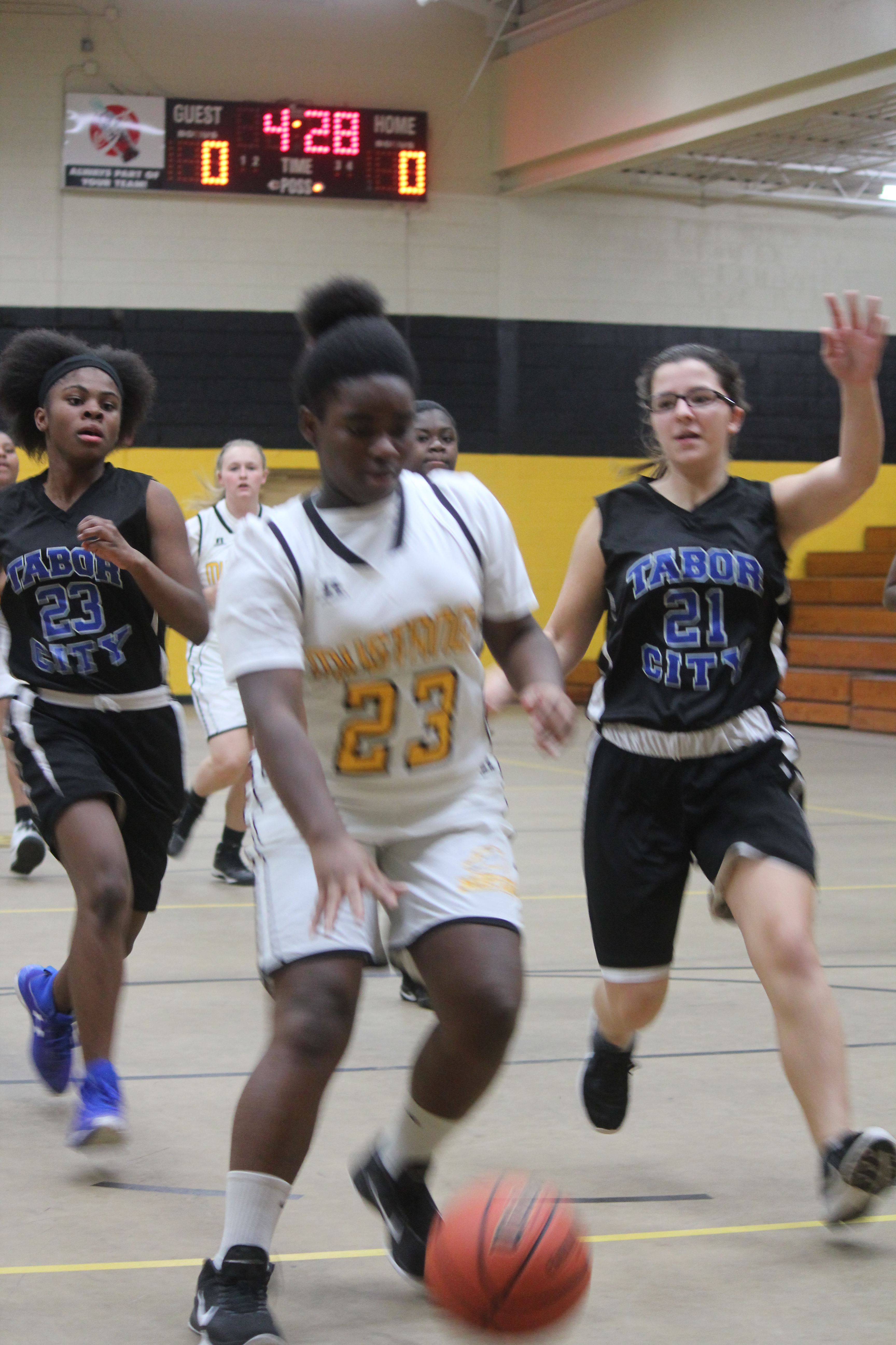 Young female basketball players dribbling and shooting hoops in a gym.