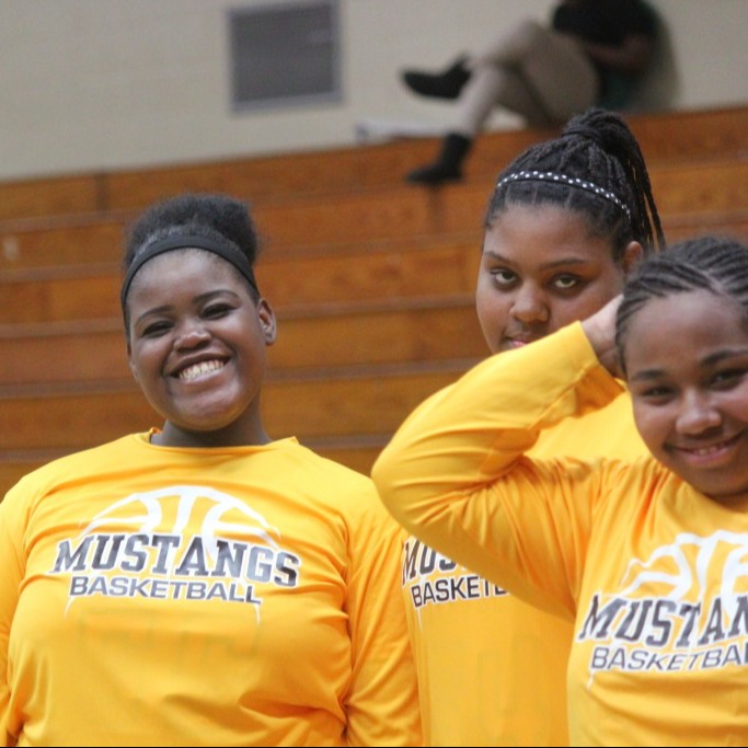 Four young women in yellow shirts smiling together.