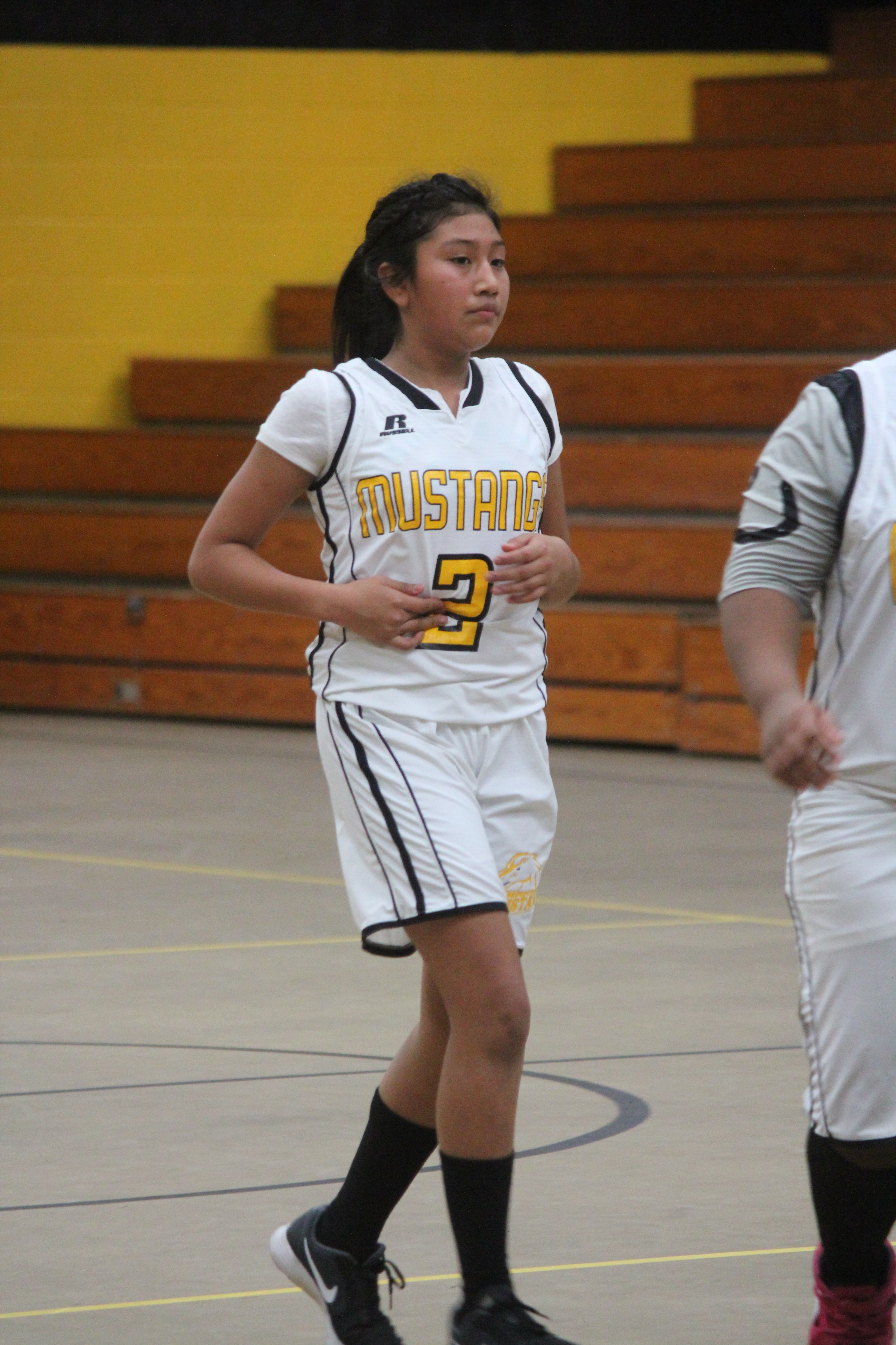 A girl basketball player wearing her white and yellow uniform.