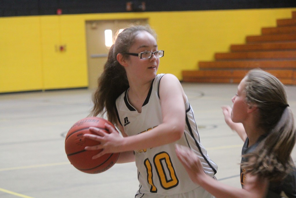 A girl in a white and yellow uniform holding a basketball.