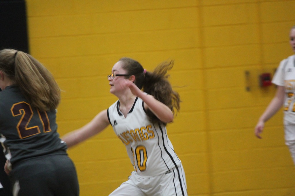 A girl in a white and yellow uniform playing basketball on a court.