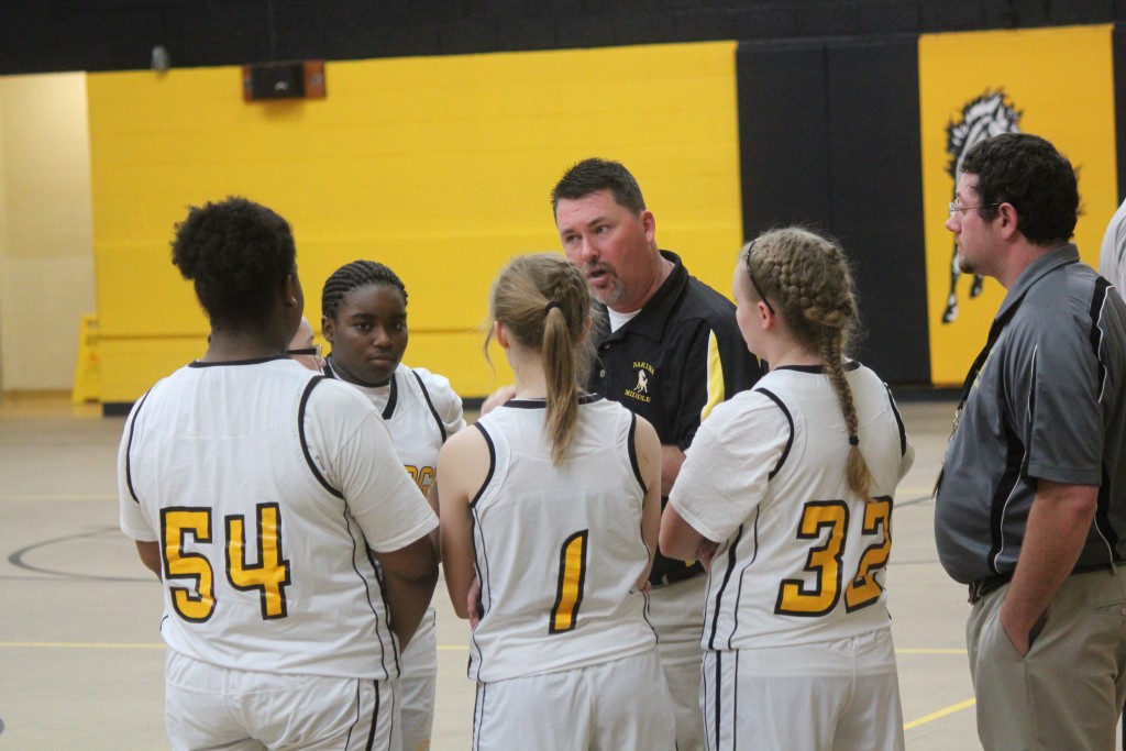 A basketball coach giving instructions to his team during a game on the court.