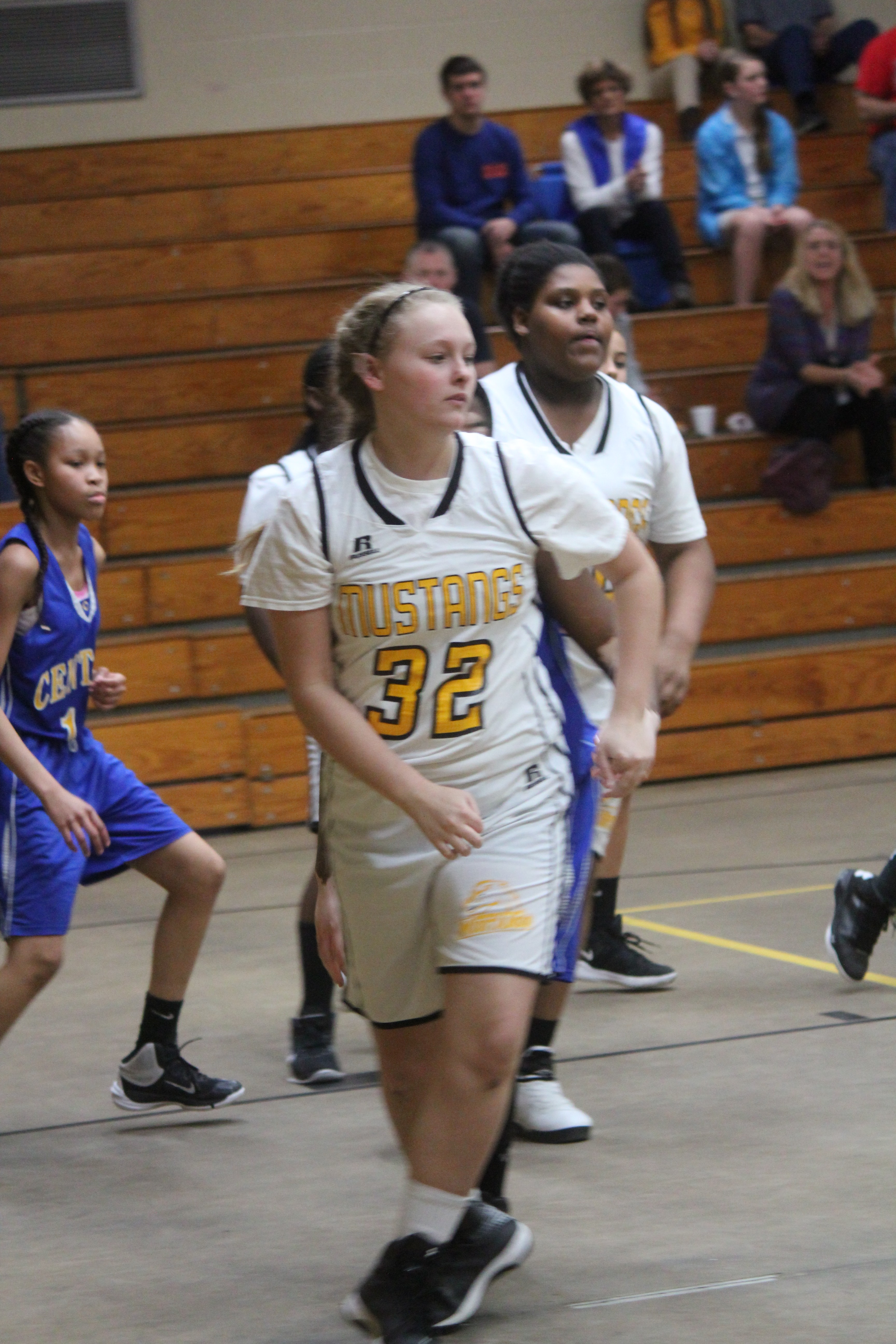 Young girl in white and blue uniform chasing basketball on court.