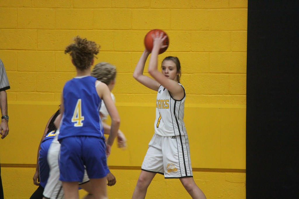 A girl in a white and yellow uniform shooting a basketball on a basketball court.