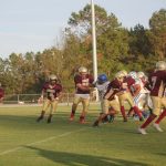 A group of athletes playing football on a grassy field.