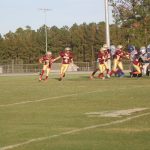 A group of athletes playing football on a grassy field.