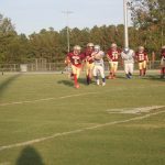 A group of athletes playing football on a grassy field.