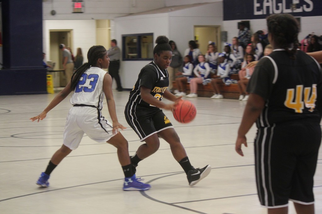 A young female athlete in a black and white basketball uniform dribbling a basketball on the court.