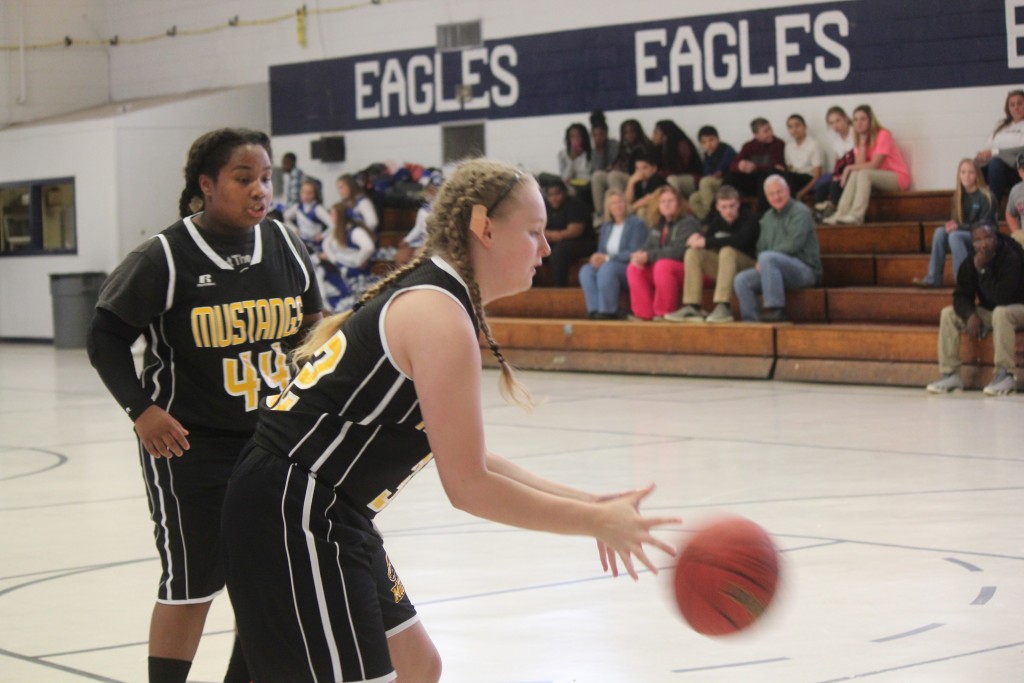 Two girls in black and yellow uniforms playing basketball on outdoor court.