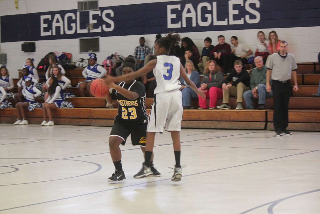 Two girls dribbling basketballs on a gymnasium court.