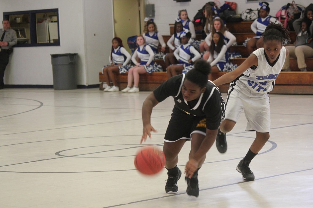 Two girls playing basketball on a court with a cheerleader cheering them on.