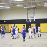 Boys playing basketball in a gymnasium, dribbling and shooting hoops.