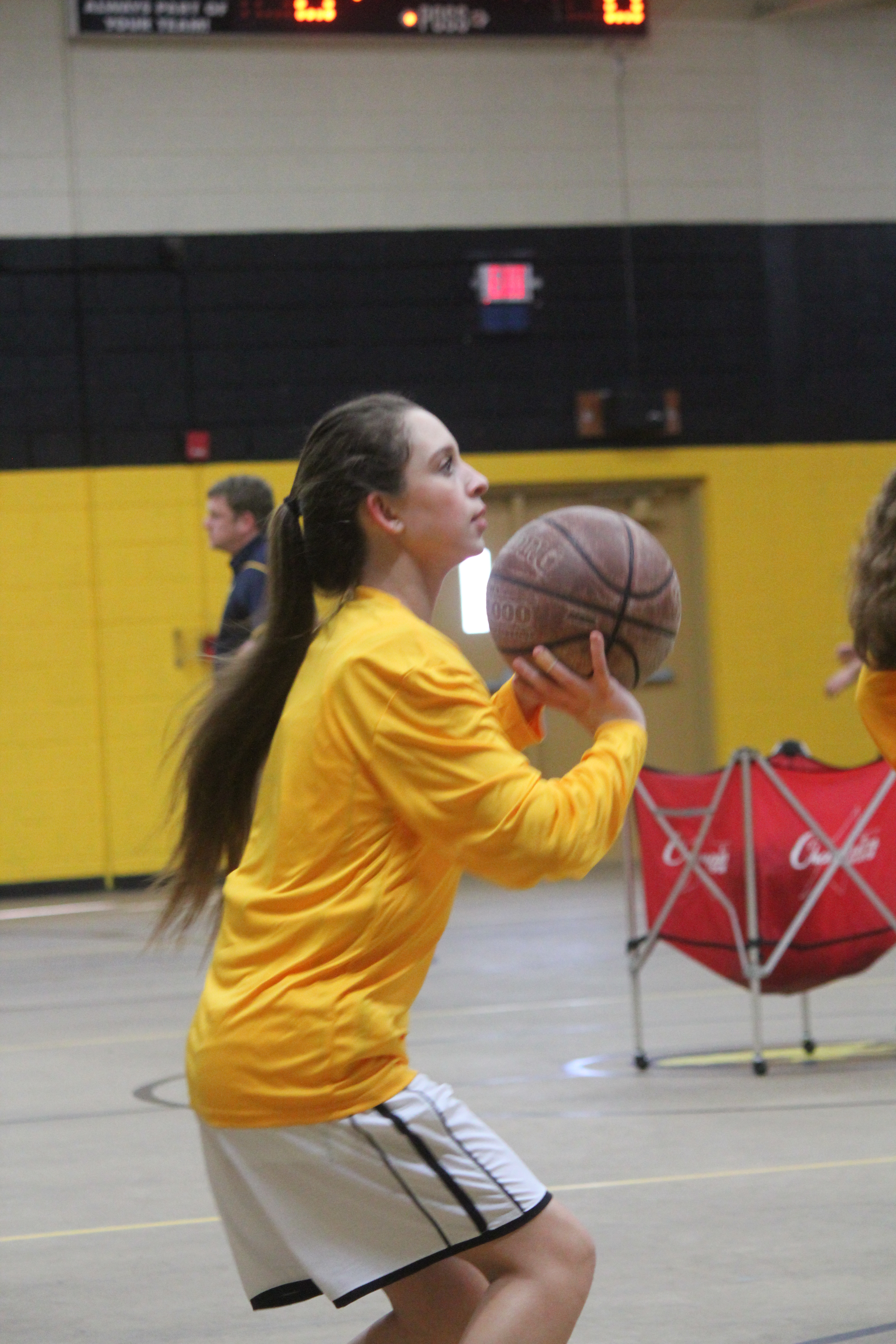 Young girl in yellow shirt holding basketball.