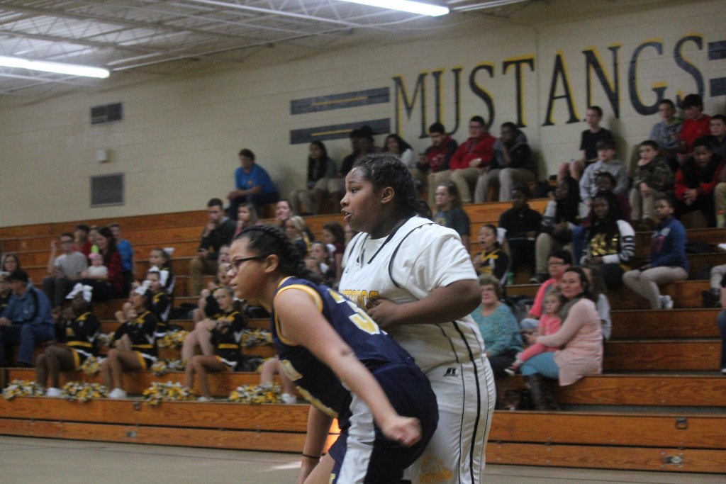 Two girls playing basketball in front of a cheering crowd.