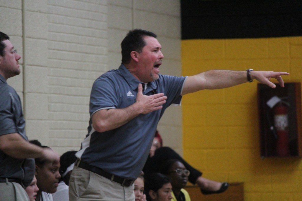 Coach pointing to sidelines as team watches attentively.